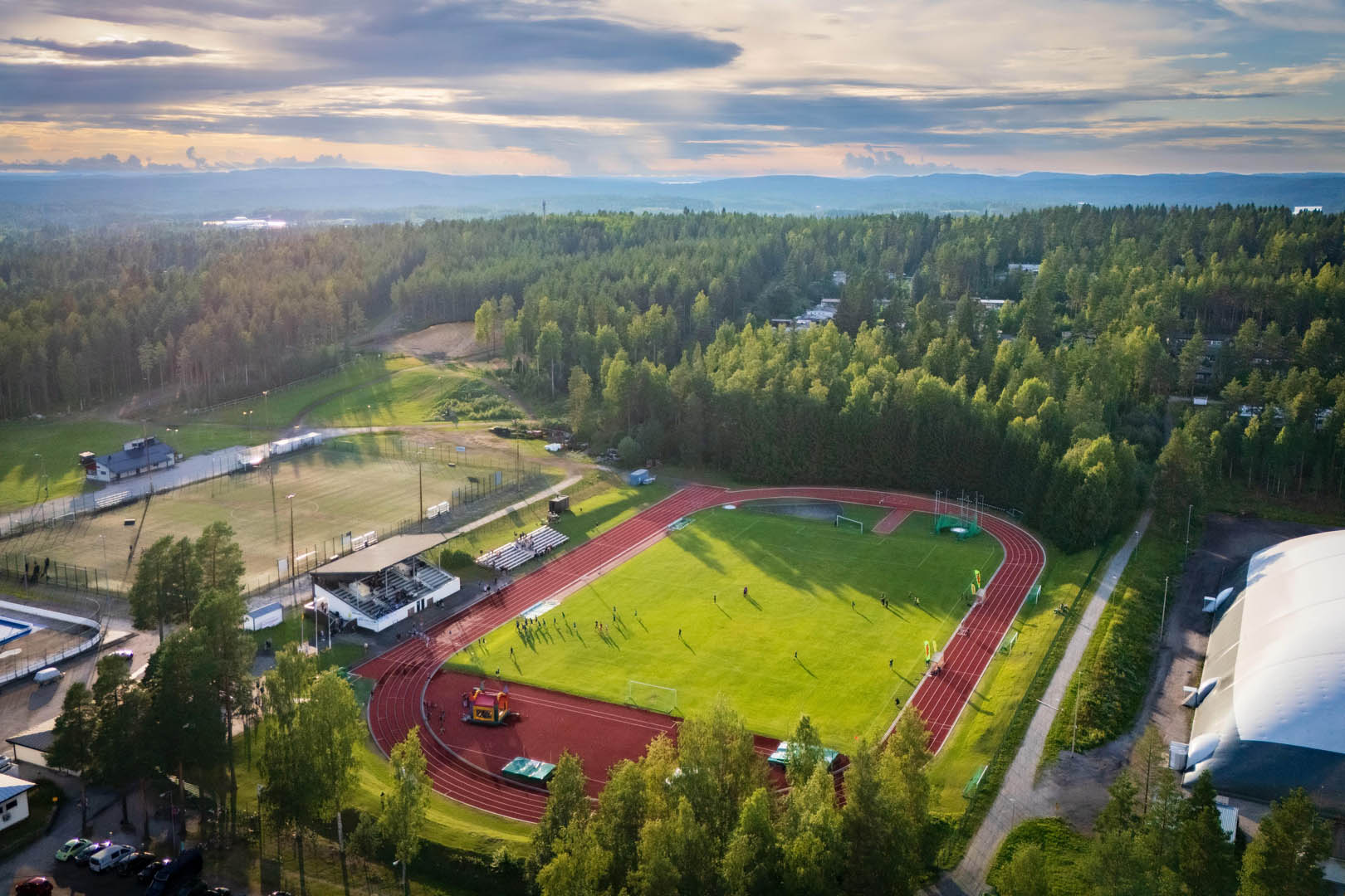 Liikuntapuiston kentät kesän vihreydessä auringonvalon siivilöityessä pilvien raoista
