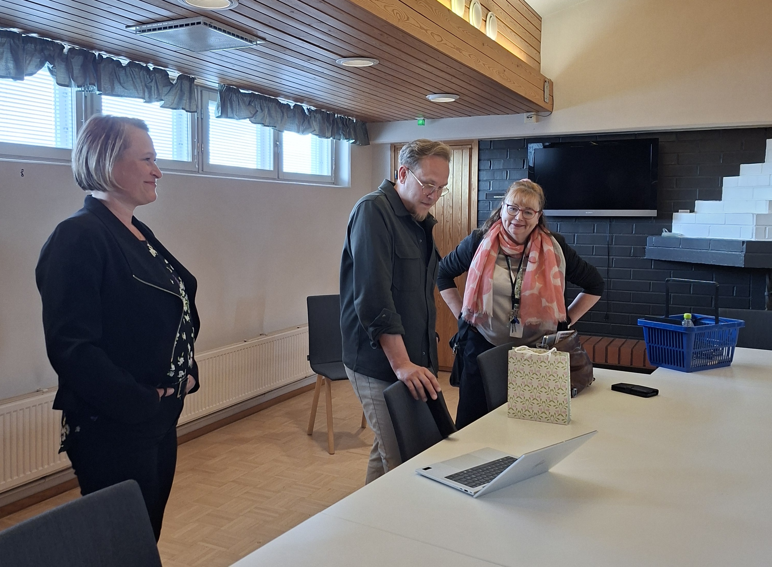 Riikka Hytönen, Lassi Puonti ja Pirjo Raittila-Parkkinen kokouspöydän äärellä katsomassa kannettavaa tietokonetta.