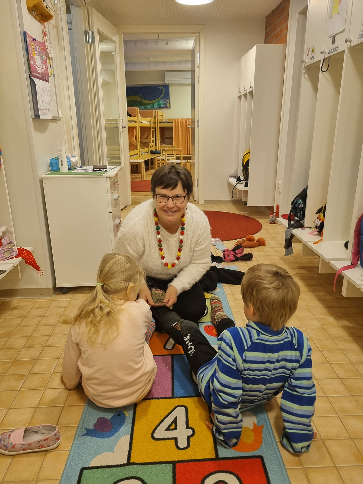 Kikka Raitanen pukee lapsia ulkovaatteisiin.