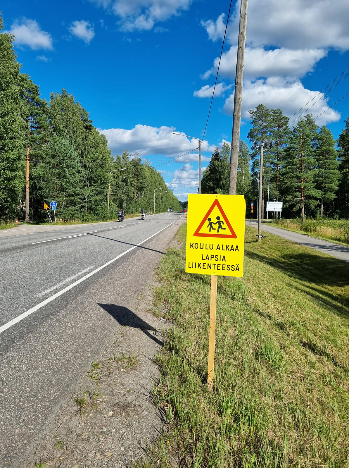 Kyltti tien varrella, jossa lukee "Koulu alkaa, lapsia liikenteessä".