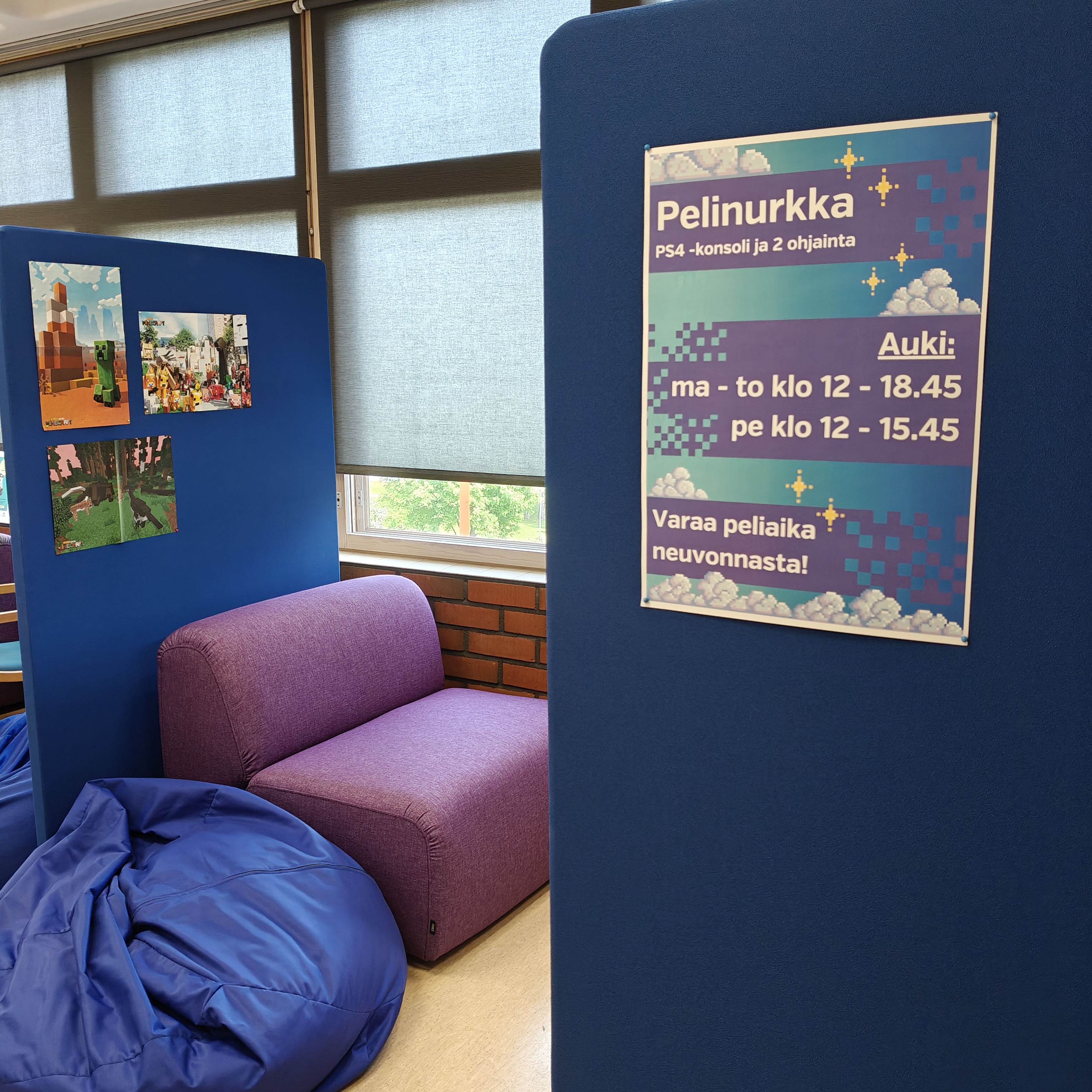 Kuva pelinurkasta. Kuvassa violetti nojatuoli, sininen säkkituoli ja kaksi sinistä sermiä. Ikkunasta näkee ulos ja sermissä lukee pelinurkan aukioloajat.